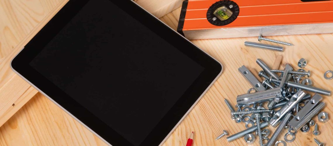 construction tool and a digital tablet lie on a light wooden table